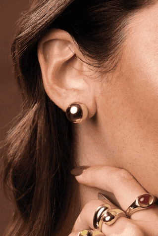 Close-up of a person wearing gold hoop earrings and rings on a brown background