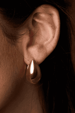 Close-up of an ear wearing a gold hoop earring with a dark background