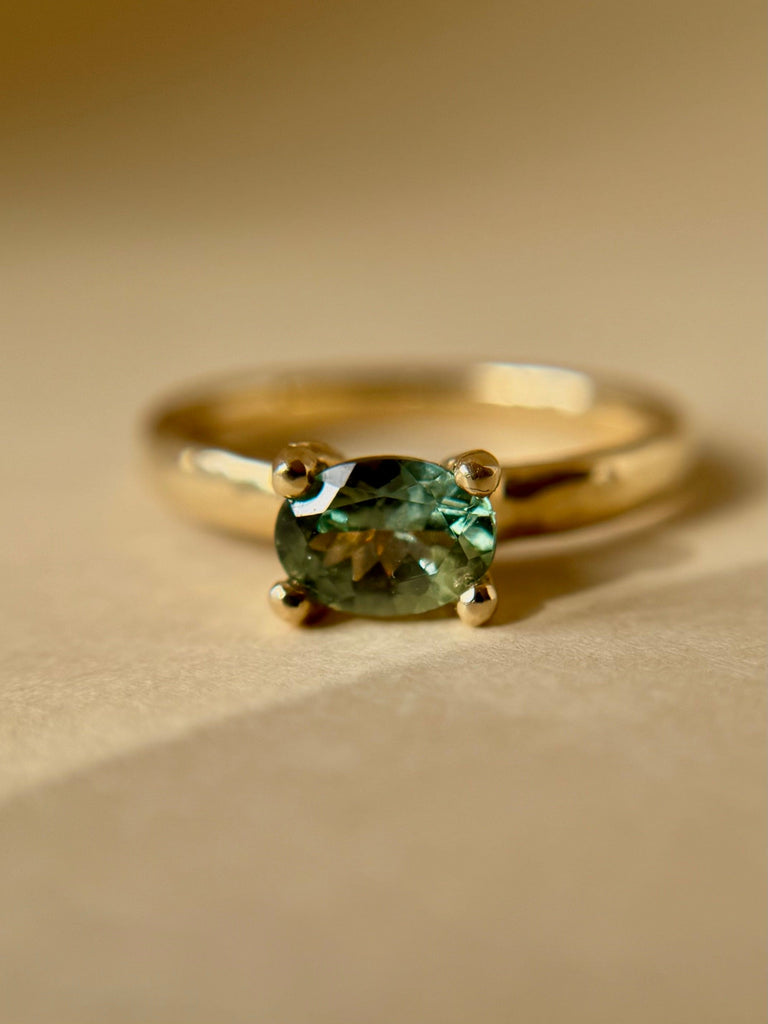 Gold ring with a green gemstone on a beige background