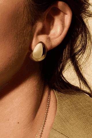 Close-up of a person wearing a gold earring with a blurred background