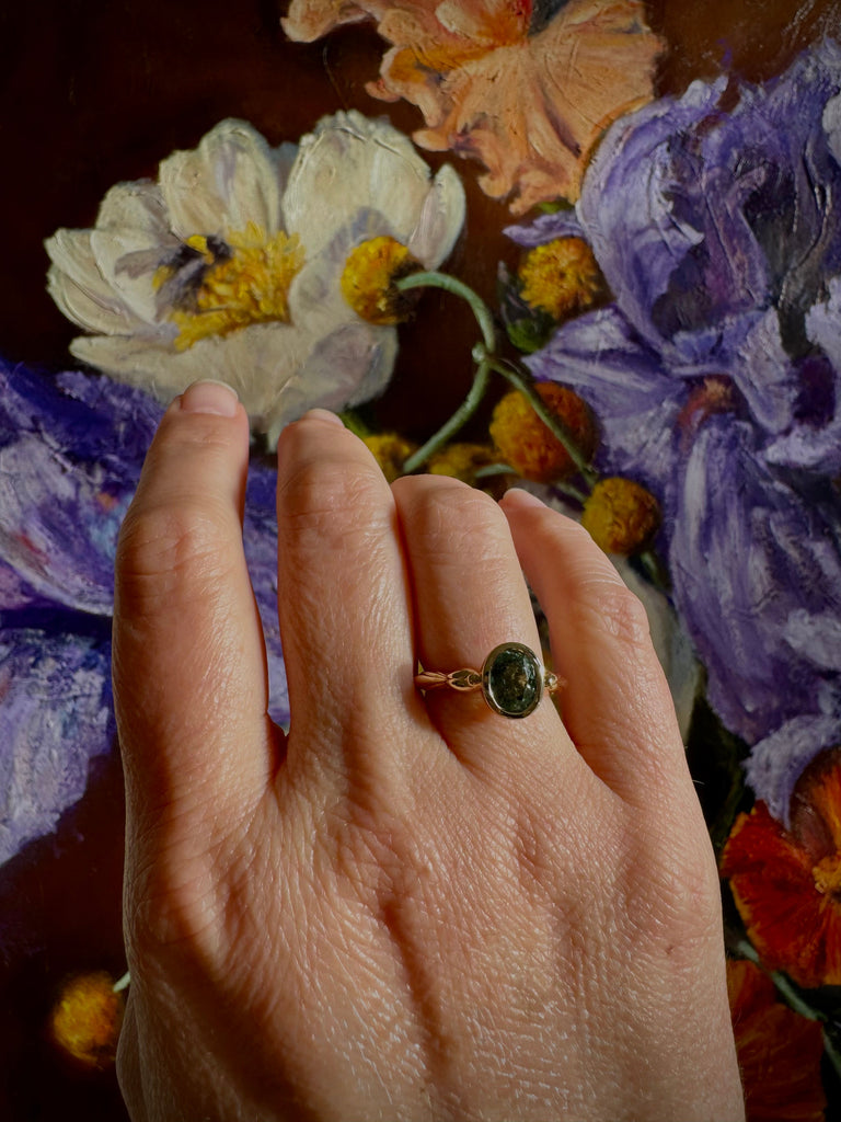 Hand wearing a ring with a floral painting in the background