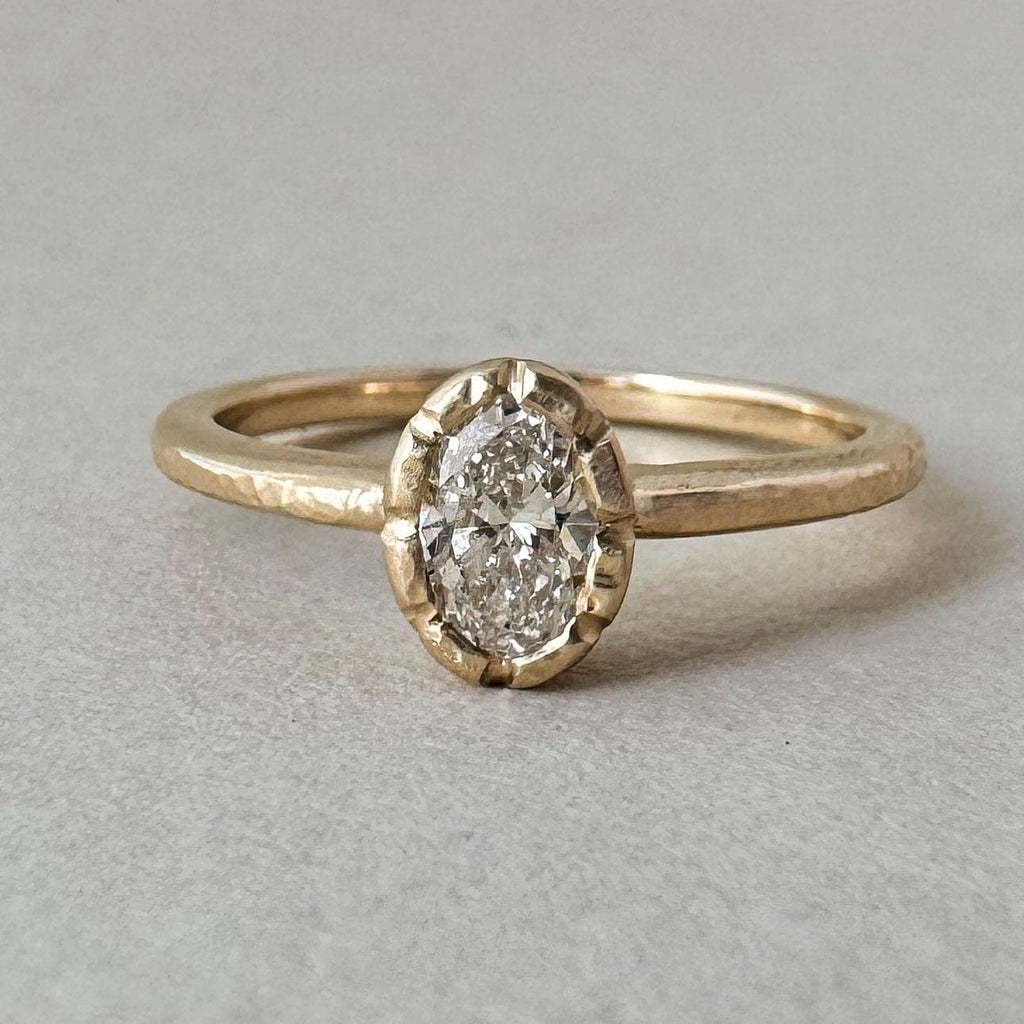 An oval lab diamond set in a unique bezel setting, resembling the petals of a wildflower. The ring's design is delicate and nature-inspired.