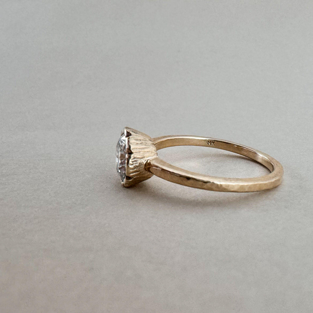 A round diamond ring with a gold bezel setting, featuring a yellow gold band with a hammer texture and a single diamond centerpiece.