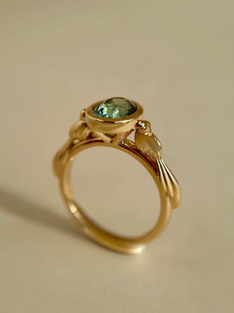 Gold ring with a green gemstone on a beige background